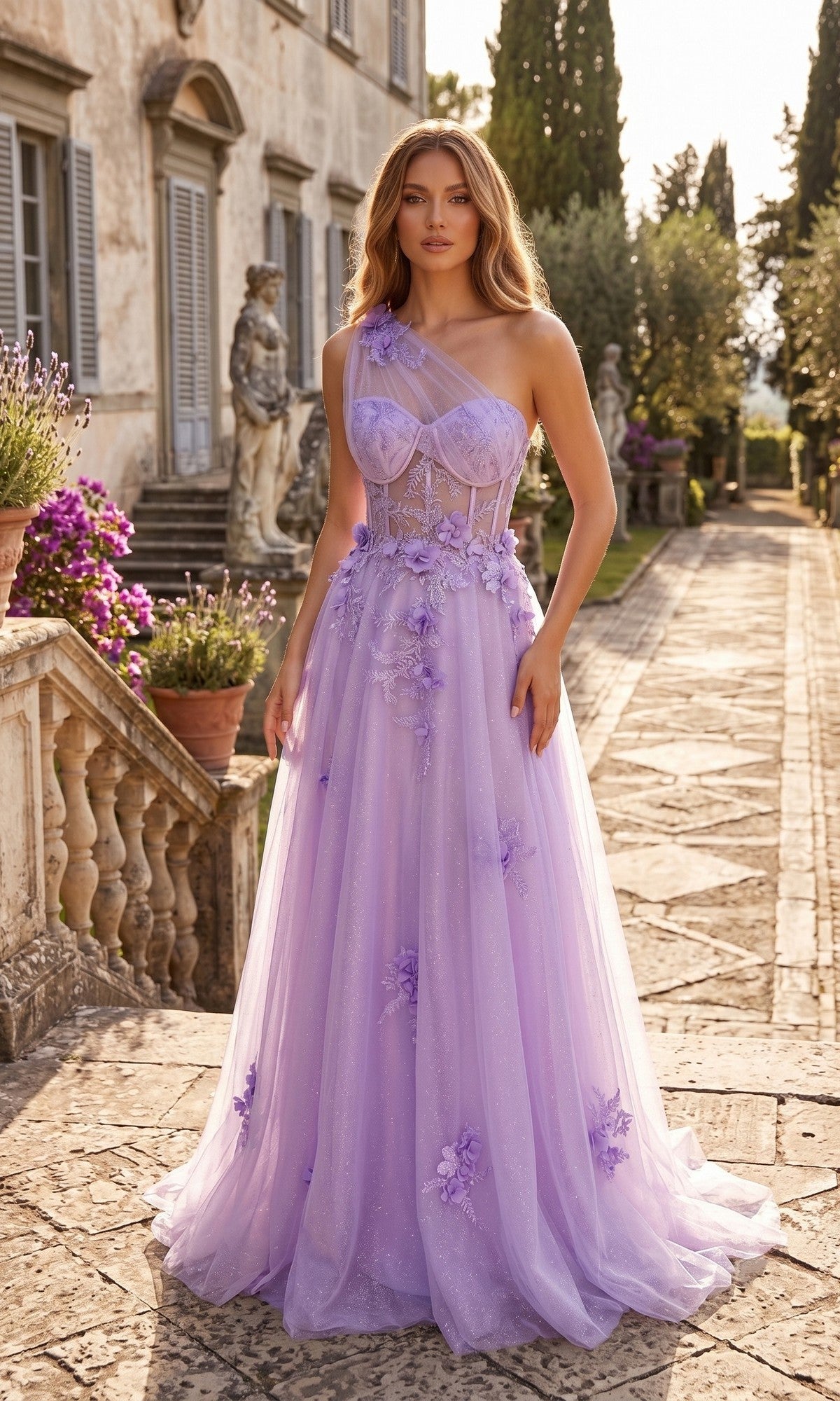 A woman stands outdoors in front of a stone building, surrounded by a stone walkway and greenery, wearing the Long Prom Dress: Chicas YG5028—a sheer lavender one-shoulder gown adorned with floral appliqué and featuring an elegant A-line glitter tulle skirt.